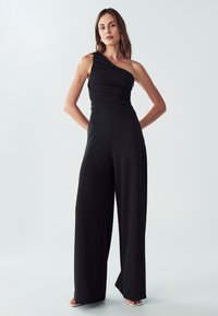 Jednoročná čierna kombinéza s nahrnutým telom, širokými nohavicami a hladkou textúrou látky. Obsahuje priliehavý pás pre zvýraznenie tvaru.