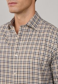Camisa de manga corta con botones en un patrón de cuadros en beige, marrón y azul marino. Cuenta con un cuello clásico y una tapeta de botones estándar. Material de algodón.
