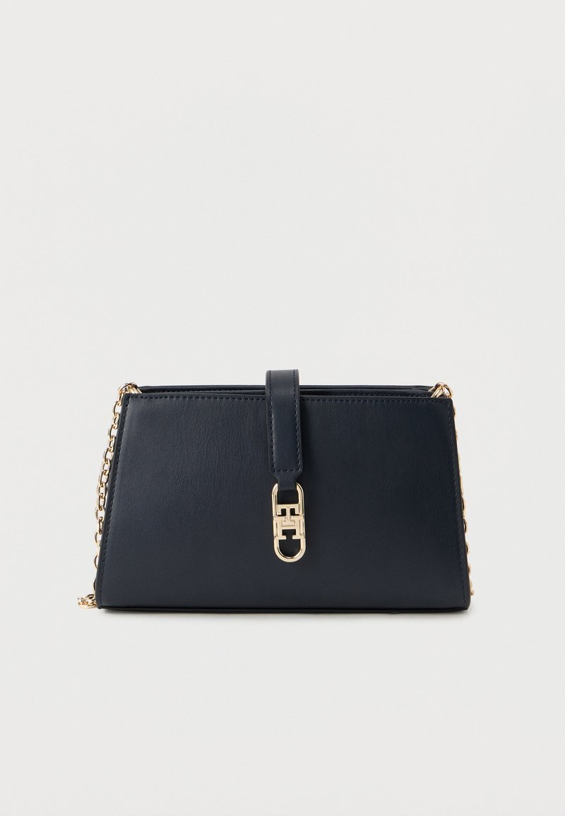 Σκουρομπλε δερμάτινο τσαντάκι χειρός με αλυσίδα λαβής σε χρυσή απόχρωση και εμπρόσθιο κλείσιμο. Διαθέτει λεία υφή και γωνιώδες σχέδιο.