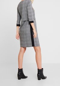 Grå och svart rutmönstrad klänning med trekvartslånga ärmar, svarta sidopaneler och en figursydd silhuett. Bärs med svarta ankelskor.