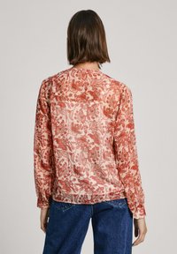 Helle blouse med et blomstermønster i nuancer af rød og creme, med lange ærmer og en samlet nederkant.