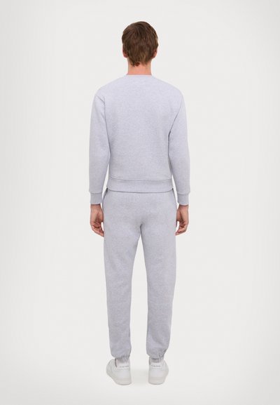 Sudadera de algodón gris con puños acanalados, combinada con joggers a juego que tienen tobillos elásticos. Modelo visto desde la espalda.