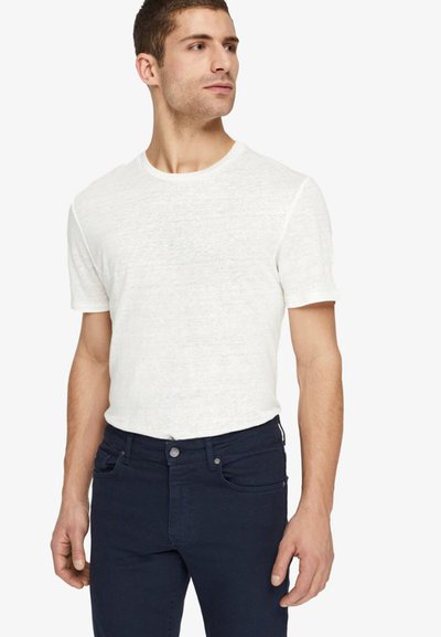 Tricou alb cu mânecă scurtă dintr-un material texturat, asortat cu blugi slim-fit de culoare bleumarin închis, având închidere clasică cu nasture și fermoar.