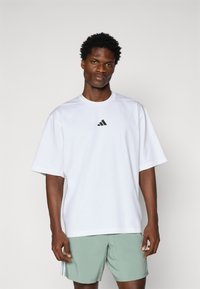T-shirt blanche à manches courtes en tissu doux avec un petit logo Adidas noir sur la poitrine, associé à un short vert menthe.
