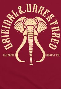 Camiseta marrón con un gráfico de elefante en color crema, con un detallado tronco y colmillos, acompañado de texto en negrita de estilo vintage.