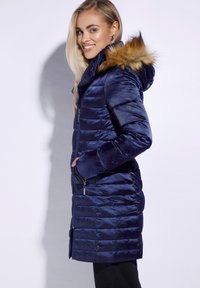 Jūras spēku krāsas pūkains žakets ar rāvējslēdzēju priekšpusē, kapuce ar mākslīgās ādas oderi un ribota apakšmala. Iespējas quilted tekstūra un divas sānu kabatas.