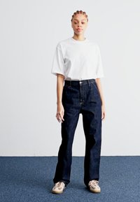 White short-sleeve t-shirt paired with high-waisted dark denim jeans. Loose fit, five-pocket design, with contrasting stitching and fly.