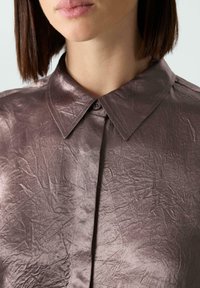 Metallisch mauvefarbene Bluse mit Kragen, aus zerknittertem Stoff, verfügt über eine durchgehende Knopfleiste, glatte Textur und spitzes Kragen-Design.