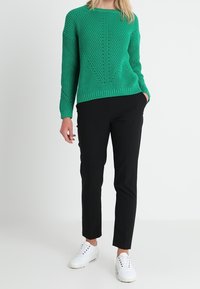 Groen gebreid sweater met een textuurpatroon, gecombineerd met zwarte op maat gemaakte broeken en witte sneakers. De sweater heeft een ronde hals en een geribbelde zoom.