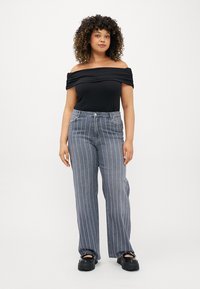 Top preto sem alças com tecido franzido; jeans de perna larga cinza às riscas com detalhe de costura discreto; sapatos de plataforma pretos.