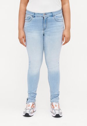 Light blue skinny jeans made of denim, featuring a classic five-pocket design and a zip-fly closure. Worn with grey and orange sneakers.