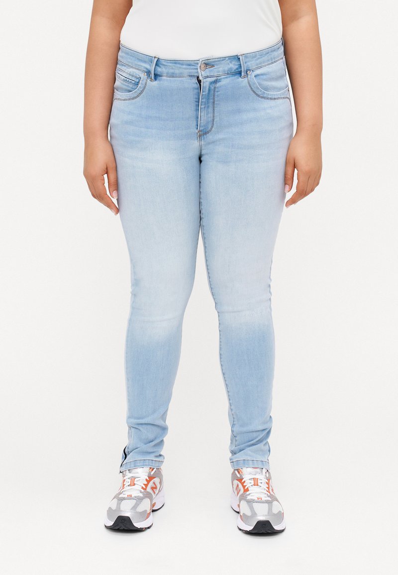 Vaqueros ajustados de color azul claro hechos de denim, con un diseño clásico de cinco bolsillos y cierre de cremallera. Combinados con zapatillas grises y naranjas.
