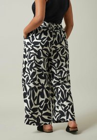 Pantalons évasés à motifs noir et blanc avec une taille élastique et des poches latérales. Tissu lisse avec des motifs abstraits en forme de feuilles.