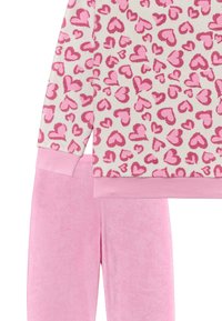 Fleece Loungewear-Set mit einem Cremetop mit pinken Herzmustern und passenden, weichen, pinken Sweatpants. Der Stoff ist strukturiert und plüschig.
