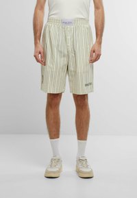 Shorts rayés vert clair et crème avec une taille élastique, fermeture par bouton et détail de logo sur la jambe gauche. Fabriqués en tissu doux.