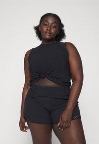 Svart atletisk topp med knuten frontdesign och ärmlös cut; ihop med svarta högmidjade shorts och subtila veckdetaljer.