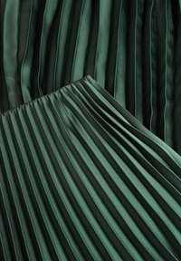 Tissu vert foncé avec de fines plis verticaux, qui se chevauchent en angle, créant une apparence texturée et stratifiée.