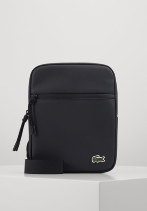 Bolso negro sintético de hombro con una superficie texturizada, bolsillo frontal con cremallera y un logo de cocodrilo verde. Incluye una correa ajustable negra.