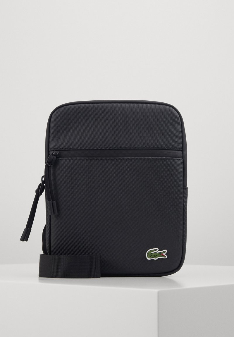 Borsa a tracolla nera in sintetico con superficie testurizzata, tasca frontale con zip e logo di coccodrillo verde. Inclusa tracolla nera regolabile.