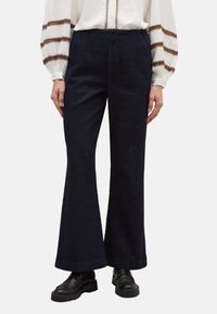 Dunkelblaue Jeans mit Schlag aus Denim, mit hoher Taille, zwei Vordertaschen und einem sauber verarbeiteten Saum. Kombiniert mit schwarzen Loafers.