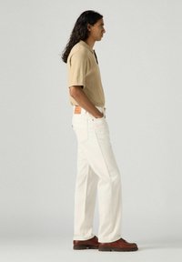 Beige short-sleeve polo shirt, white straight-leg jeans, brown leather shoes. Notable details include a rear label on jeans and shirt collar.