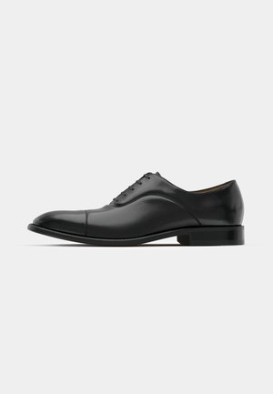 Black leather dress shoe with smooth texture, rounded toe, and five eyelets. Features a low stacked heel and subtle seam detailing.