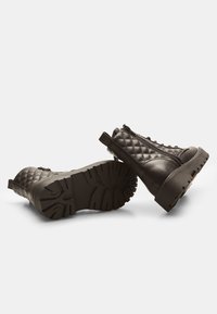 Botas de tobillo negras acolchadas con suela gruesa, que cuentan con cremalleras laterales, acentos de tirador en el tacón y un patrón de textura en la parte inferior.