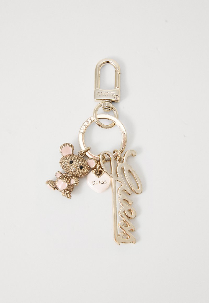 Gouden sleutelhanger met een met rhinestenen bezette berencharme, een hartlabel en het woord "Guess" in cursieve letters. Gladde, metalen afwerking.