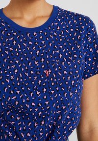 Blå t-shirt med leopardmönster i rosa och svart, rund halsringning och en liten ficka. Levi's logotyp synlig på fickan.