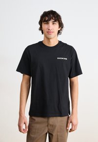 Juodas medvilninis marškinėliai trumpomis rankovėmis ir apvalia iškirpte, su baltu "DICKIES" logotipu kairėje krūtinės pusėje. Saldus paviršius.