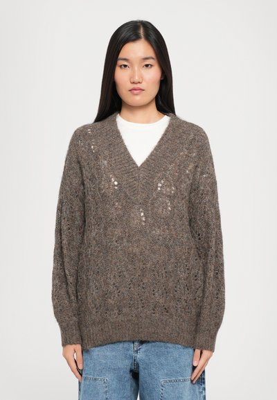 Strikket brun sweater med v-hals, der har en løs pasform og blondermønstre. Ribbet manchetter og kant, båret over en hvid skjorte og denimjeans.