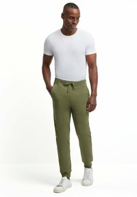 Olijfgroene sweatpants met een trekkoord in de taille, zijzakken en een gladde textuur, gecombineerd met een aansluitend wit t-shirt en witte sneakers.