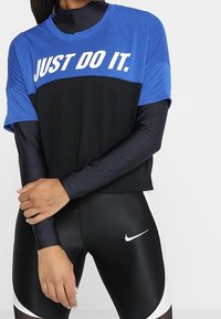 Camiseta deportiva azul y negra con el texto "JUST DO IT", de mangas cortas y textura de malla, combinada con leggings negros que presentan un logo blanco de Nike.