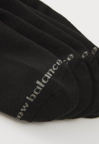 Crne čarape izrađene od mekanog, teksturiranog materijala. Sadrže bijeli „new balance“ logo otisnut sa strane. Jednostavan dizajn, bez dodatnih uzoraka.