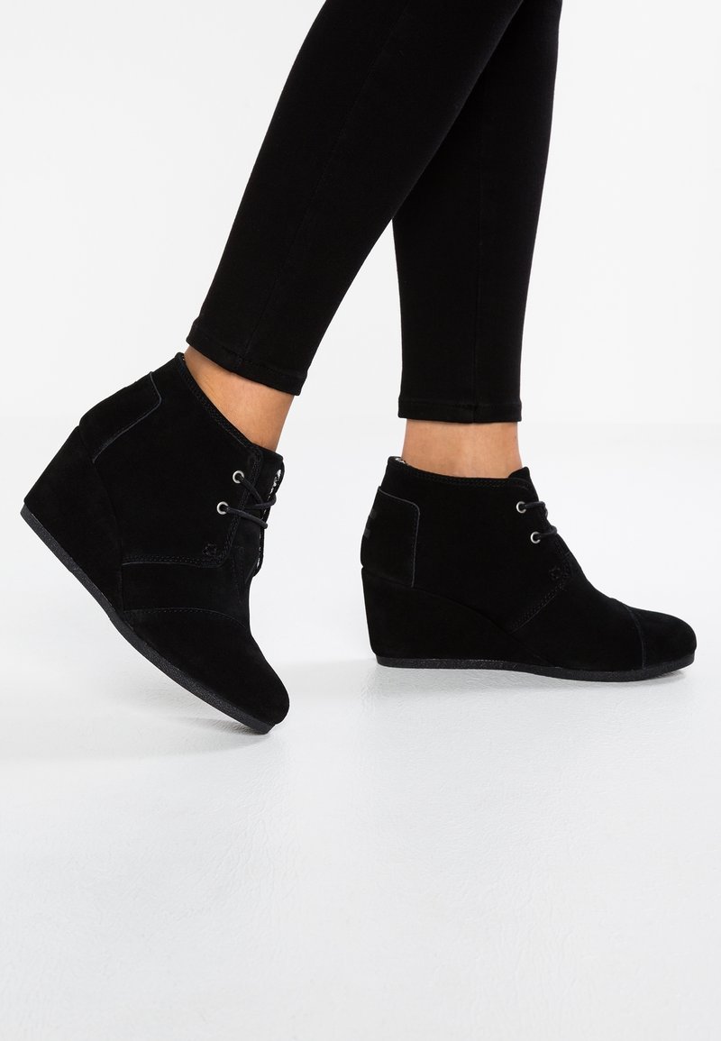 Stivaletti a wedge in suede nero con punta rotonda, dettagli cuciti, lacci anteriori e zip laterale per una facile vestibilità.