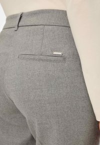 Grijze wolblend broek met een subtiele textuur, voorzien van een achterzak en een klein zilveren accentplaatje op de zak.