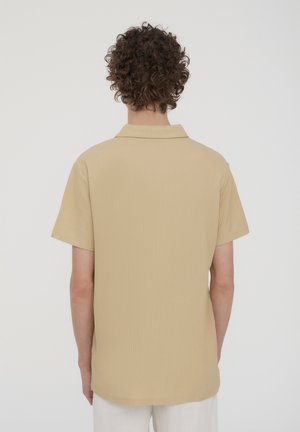 Camicia beige a maniche corte con tessuto texture, colletto sottile e orlo arrotondato. Materiale liscio e leggero, ideale per un look casual.