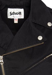 Chaqueta negra con cuello de muesca, cierre con cremallera y acentos metálicos. La etiqueta dice "Schott", con una cremallera dorada y botones a presión.