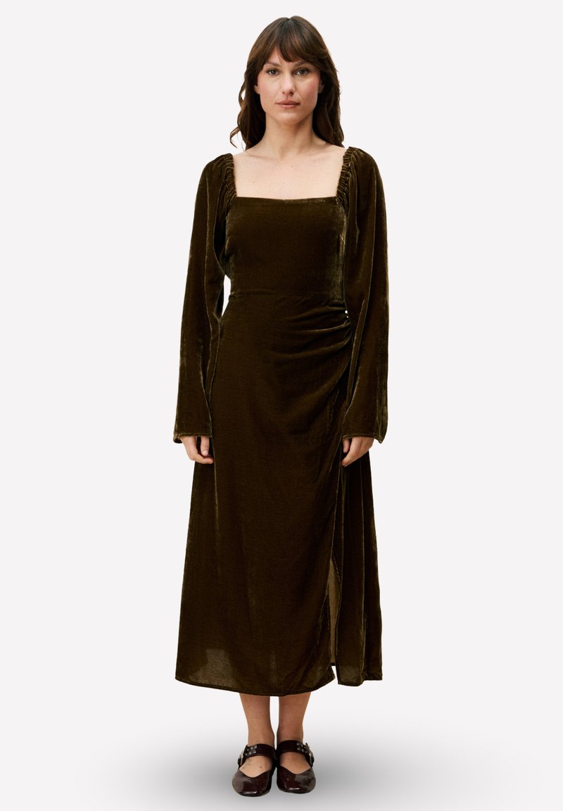 Robe longue en velours vert foncé avec un décolleté carré, un corsage ajusté et de longues manches bouffantes ; elle présente une fente latérale et un détail froncé.