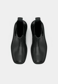 Fekete bőrből készült slip-on csizma pár négyzetes orral, felülnézetből egy fehér háttér előtt.