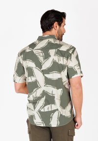 Camisa de manga corta con un patrón abstracto de hojas en verde y beige, elaborada con una tela texturizada, con dobladillo recto y cuello de botones.