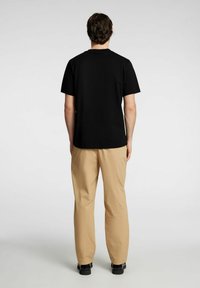 Svart kortärmad t-shirt med rund halsringning, tillsammans med beige löst sittande byxor och svarta skor. Bakgrunden är enkel vit.