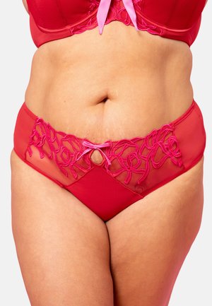 Curvy person wearing red lingerie with floral lace details and pink ribbon bows on the bra and panties against a plain background.