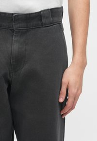 Ciemnoszare spodnie o teksturowanej tkaninie, charakteryzujące się prostym krojem, standardowym pasem i kieszenią z przodu po lewej stronie.