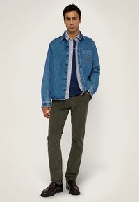 Kurtka dżinsowa w jasnoniebieskim kolorze, zapinana na guziki, z kieszenią na piersi; nałożona na granatową koszulę. Stylizację uzupełniają oliwkowozielone spodnie i ciemne buty.