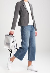 Blazer grigio a righe sottili sopra una maglietta bianca, abbinato a jeans blu cropped e sneakers bianche. Zaino argentato con spallacci neri.