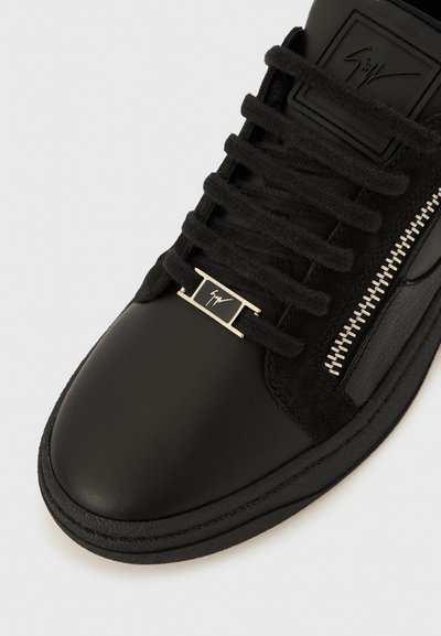 Black leather and suede sneaker with black laces, silver zipper detail, and a metal lace tag featuring a signature logo.