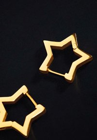 Orecchini a forma di stella dorata con una finitura lucida. Il design è geometrico, con punti acuti e un interno aperto.