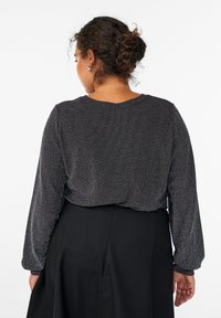 Črn dolg rokav s herringbone vzorcem, okoli okroglega ovratnika in z nabranimi rokavi; oblečen čez enobarvno črno krilo.