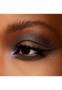 Nahaufnahme eines Auges mit verblendetem dunklem Lidschatten in Brauntönen und Schwarz, ergänzt durch einen Hauch von lila Schimmer entlang des unteren Wimpernkranzes.